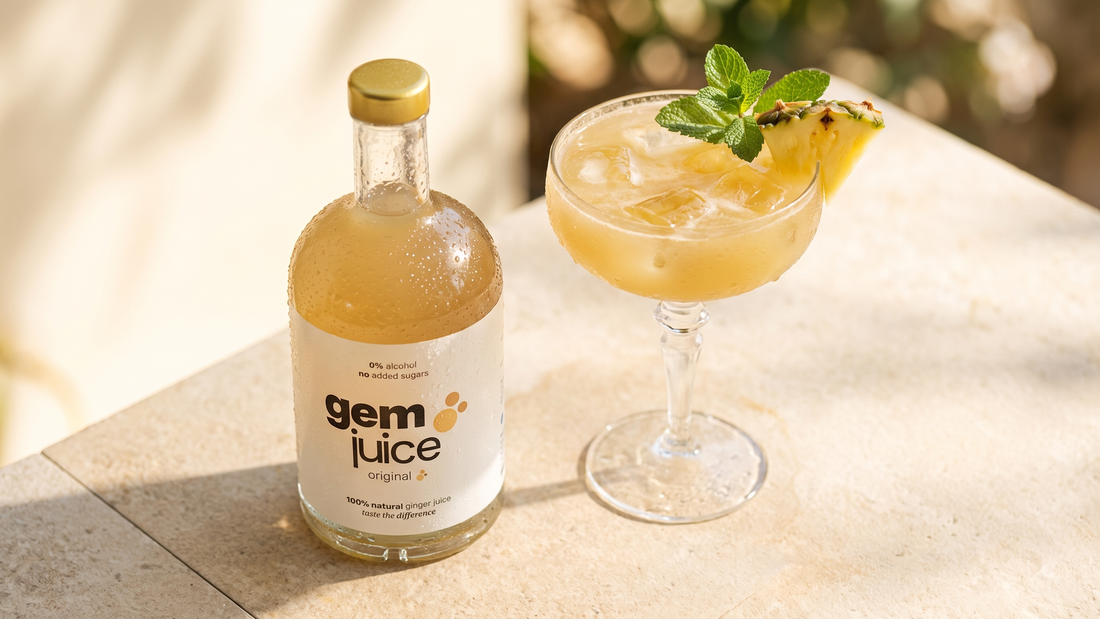 Tall coupe glass of pineapple ginger cooler with Gem Juice Original, garnished with pineapple wedge and mint, on a bright summer surface