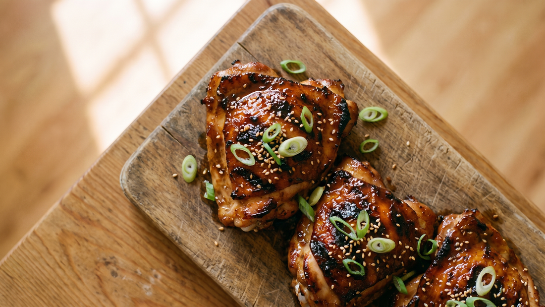 Top-down photo of sticky Gem Juice glazed grilled chicken thighs on a plate, garnished with scallions and sesame seeds