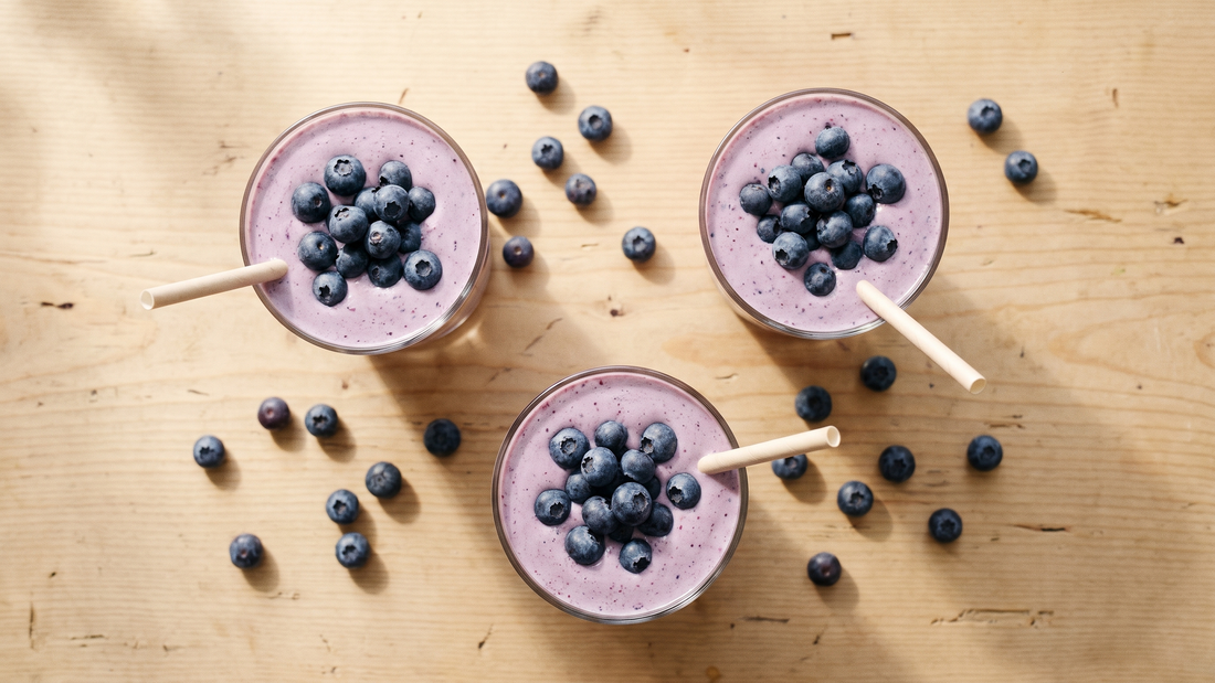 Three glasses of blueberry ginger milkshake shot from directly overhead on a wooden surface with scattered blueberries