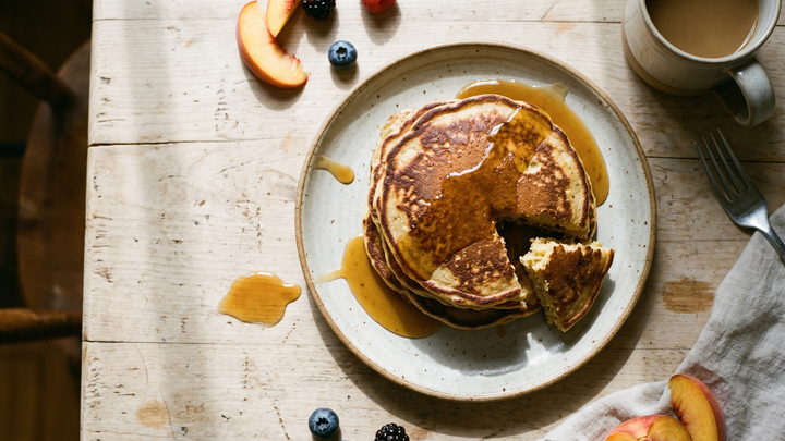 Overhead shot of a stack of golden ginger pancakes with warm honey ginger drizzle, fresh berries and grated ginger, on a rustic wooden table