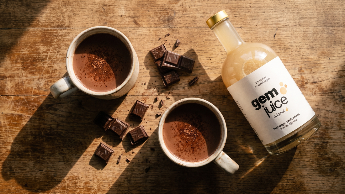 Two mugs of Ginger Hot Chocolate on a wooden table in warm evening light, with a bottle of Gem Juice Original beside them