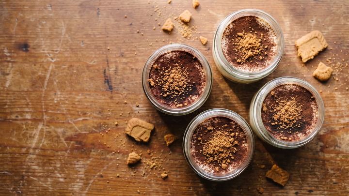 Four jars of speculoos ginger tiramisu dusted with cocoa and crushed speculoos, seen from above on a weathered wooden table