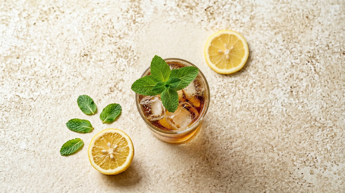 Golden ginger lemonade spritz over ice with fresh mint, lemon halves on a stone surface