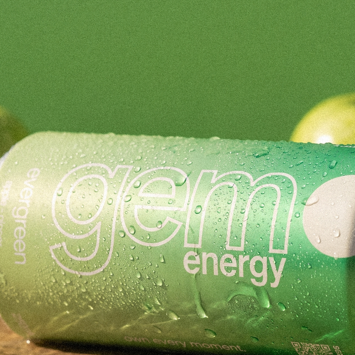Close-up of a chilled Gem Energy Evergreen can lying on its side next to green apples