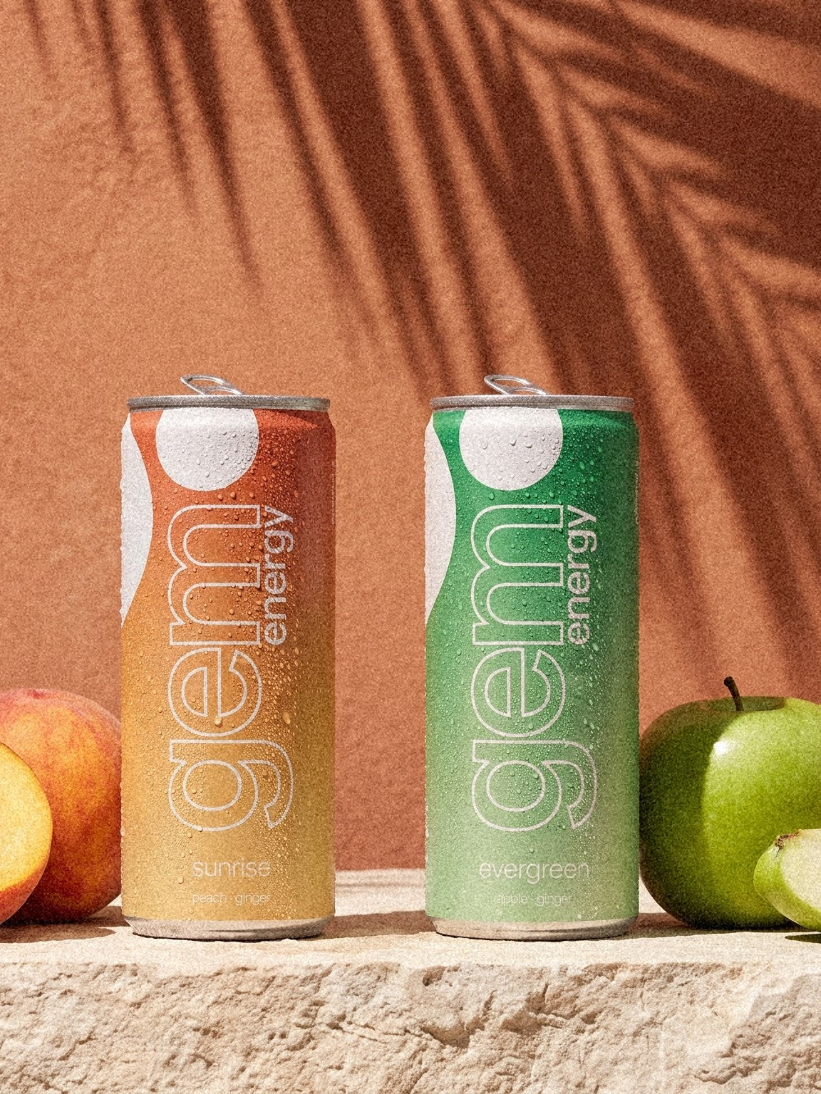 Gem Energy Sunrise and Evergreen cans with peach and apple on a sunlit terracotta wall
